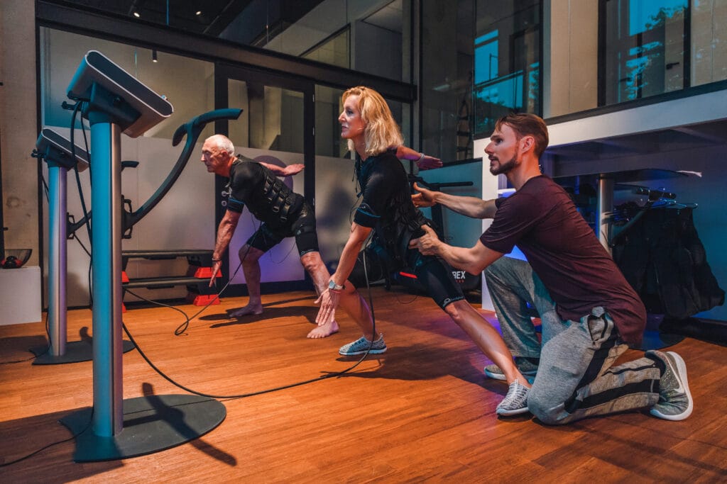 Twee deelnemers die sporten met elektroden. Ze voeren een oefening uit onder persoonlijke begeleiding van een personal trainer