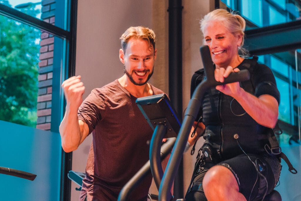Een EMS trainer die een een vrouw aanmoedigt tijdens haar EMS training op de crosstrainer